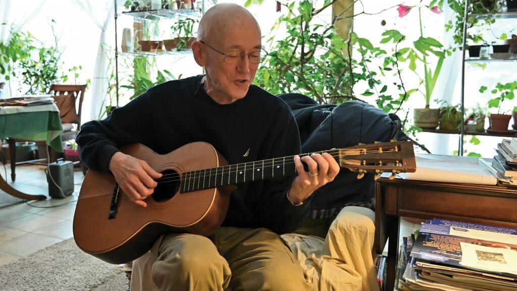 Rick Exner playing his guitar in his house