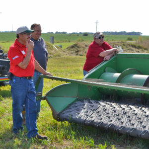 Attendees stand near a tractor as they listen to their host during a field day. 