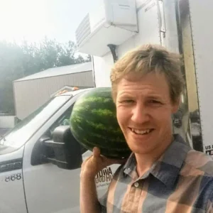 Peter Kraus holding a watermelon in front of a Iowa Food Hub delivery vehicle. 