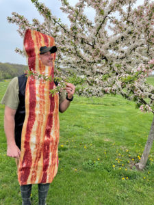 Ethan Book sports a bacon costume while standing next to a blooming fruit tree on his farm. 