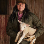 Wendy Johnson poses for the camera in a barn with a lamb in her arms. 