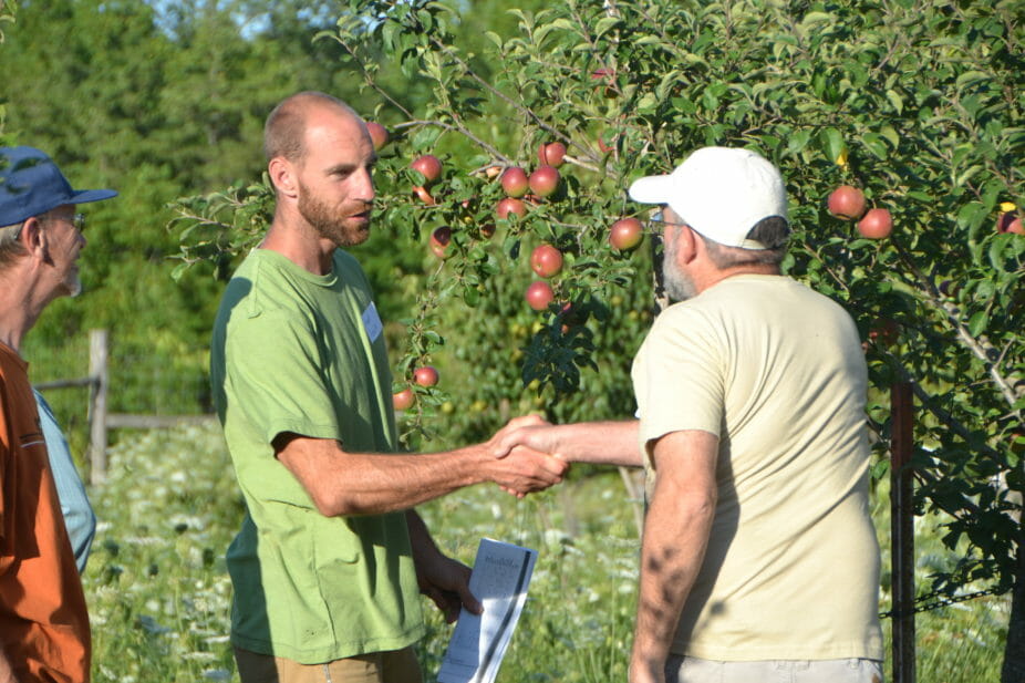 Grant Schultz and Jack Knight greet each other by an apple tree.