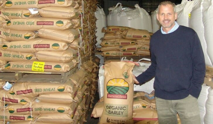 Speaker Mac Ehrhardt poses with wheat and barley seed at Albert Lea Seed House