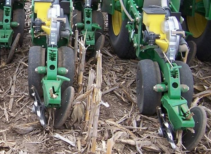 On a planter we can see two gauge wheels that cup in to a smaller diameter where they meet over the seed trench and the closing wheels show one spiked metal wheel on the left and a smooth rubbery wheel on the right.