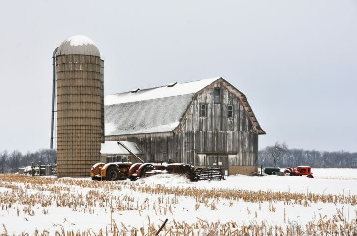 Snowy barn and silo with several tractors parked in front