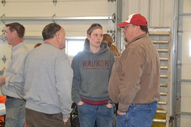 A man on the right in an ISU baseball cap chats with a young woman and man in a garage space.